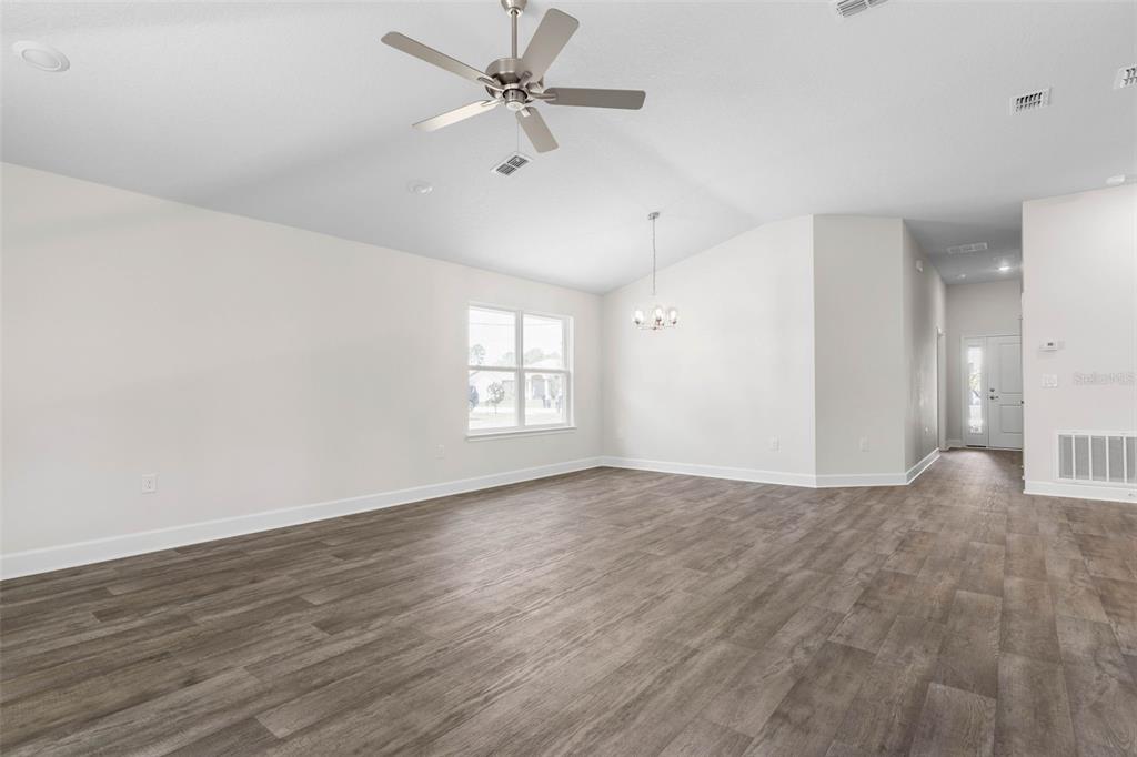 A spacious, empty room features light gray walls, wood-look flooring, a ceiling fan, and windows — 23 PRETORIA LANE, PALM COAST, FL