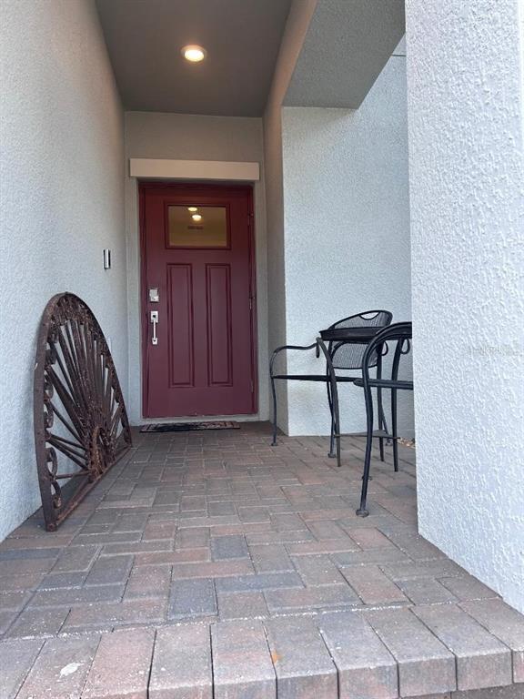 A red front door opens onto a brick-paved entryway with metal chairs and decor — 16919 FORGE SURF STREET, LAND O LAKES, FL