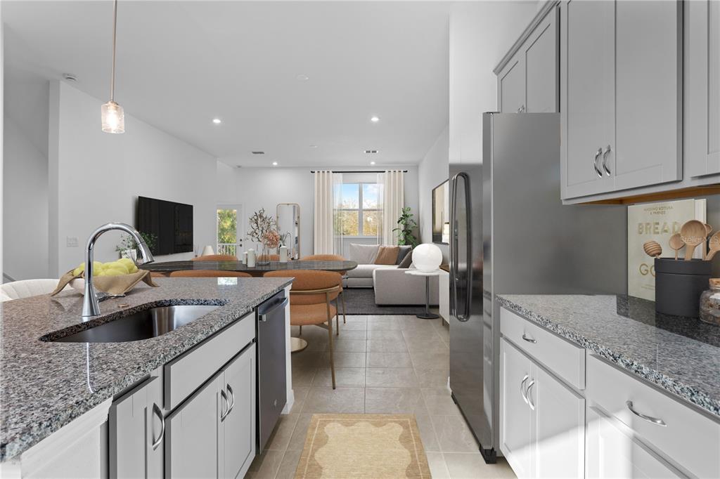 A kitchen with granite countertops and gray cabinets opens into a living and dining area — 9616 MONTAGUE STREET, WESTCHASE, FL
