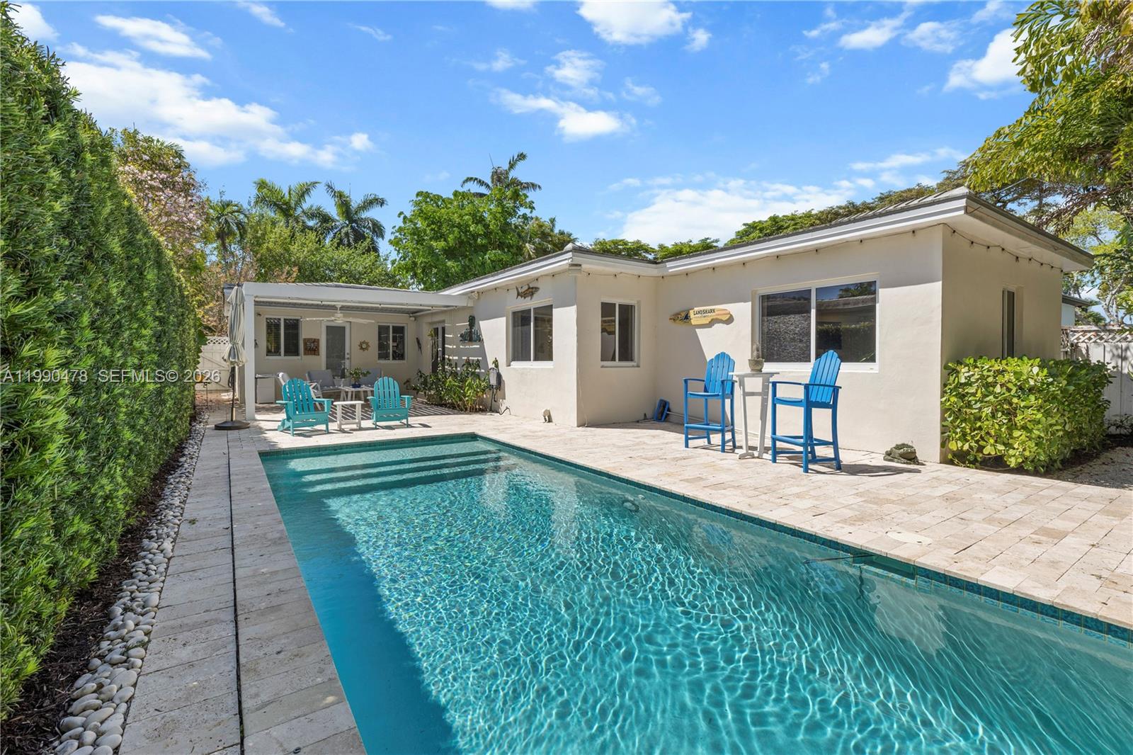 A swimming pool sits on a stone patio beside a single-story house with blue chairs — 711 NE 72nd Ter, Miami FL 33138, MIAMI, FL