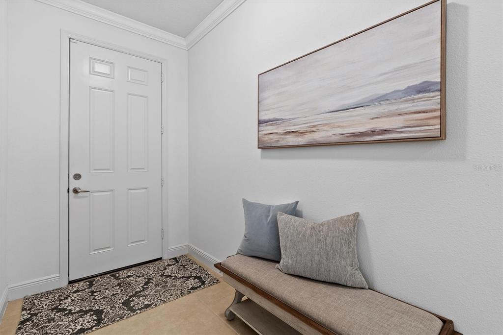 An entryway features a white door, a patterned rug, and a bench with two pillows — 7526 RIDGELAKE CIRCLE, BRADENTON, FL