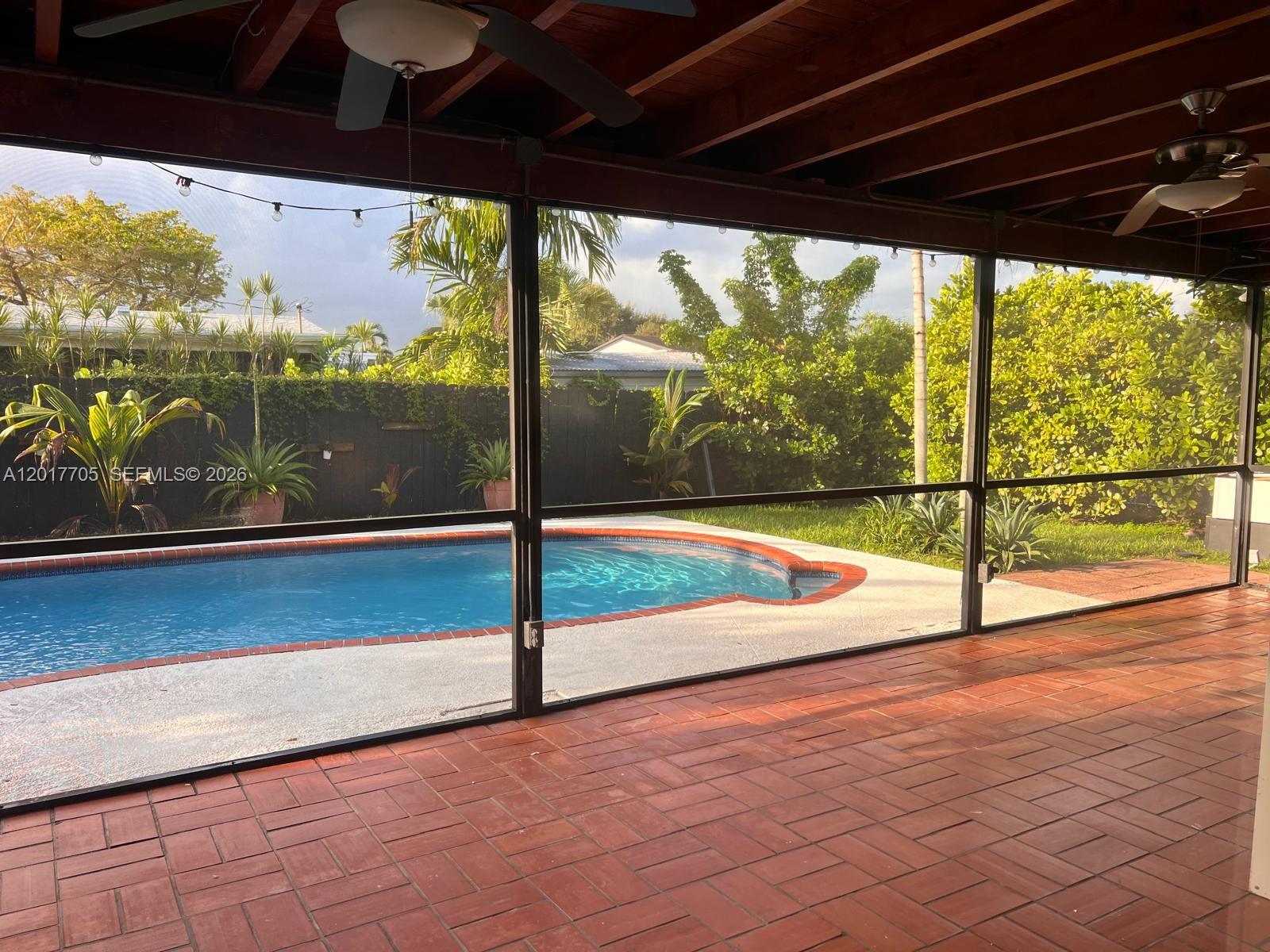 A screened-in patio overlooks a swimming pool with a brick deck and lush landscaping — 9770 SW 77th Ter, Miami FL 33173, MIAMI, FL