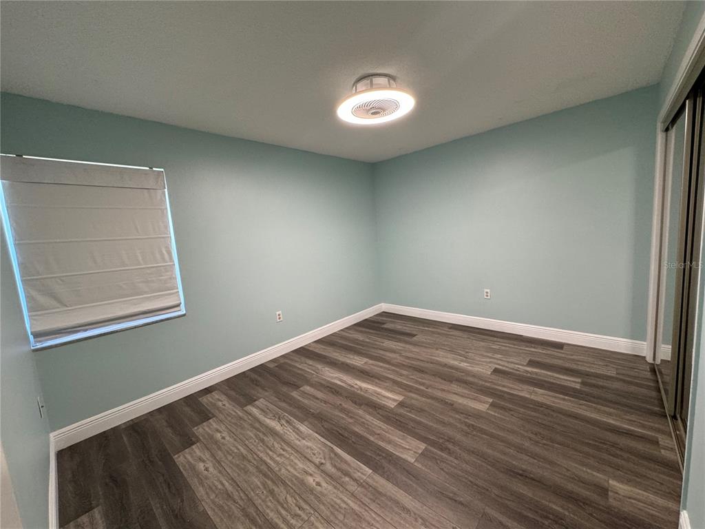 An empty bedroom with light blue walls, wood-look flooring, and a modern ceiling light fixture — 700 E AIRPORT BOULEVARD UNIT G4, SANFORD, FL