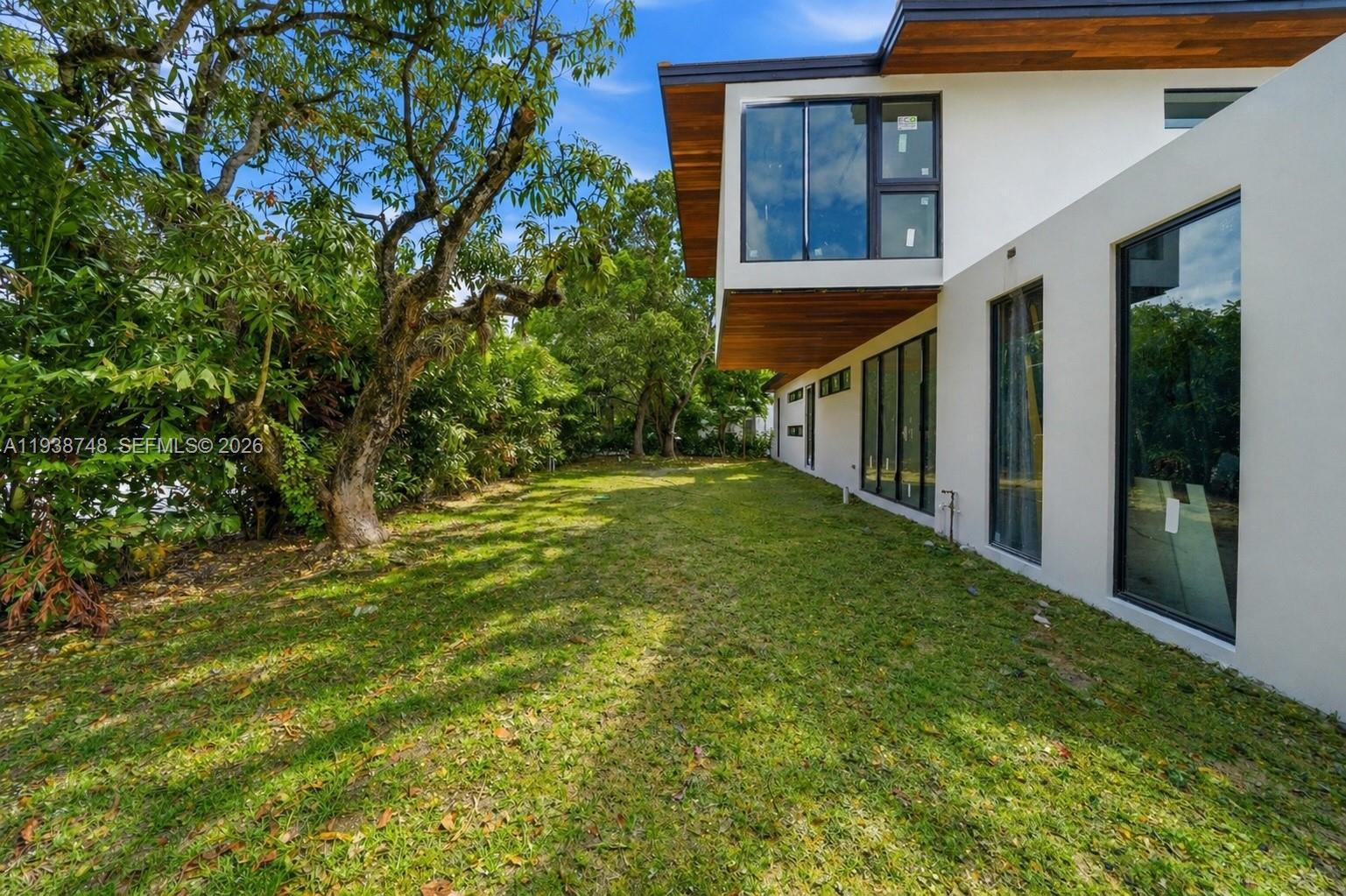 A modern white house with large windows overlooks a grassy backyard with mature trees — 4150 Loquat Ave, Miami FL 33133, MIAMI, FL