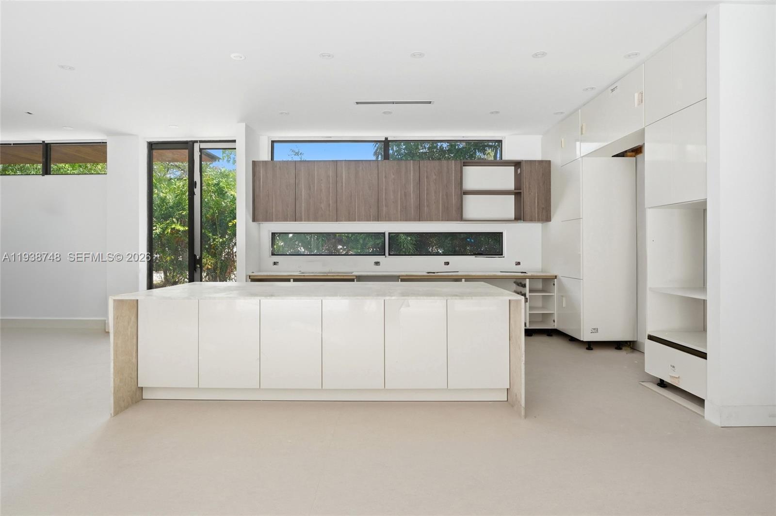 A modern kitchen features a white island, wood-toned upper cabinets, and large horizontal windows — 4150 Loquat Ave, Miami FL 33133, MIAMI, FL