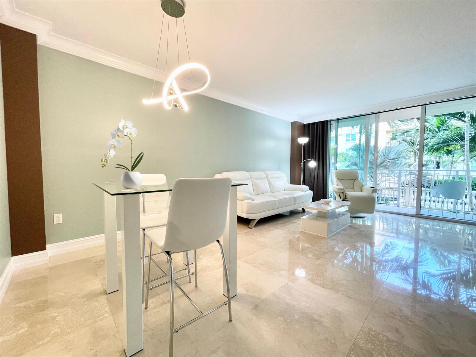 A modern living and dining area features light green walls, white furniture, and marble flooring — 99 SE Mizner Boulevard # 736, Boca Raton FL 33432, BOCA RATON, FL