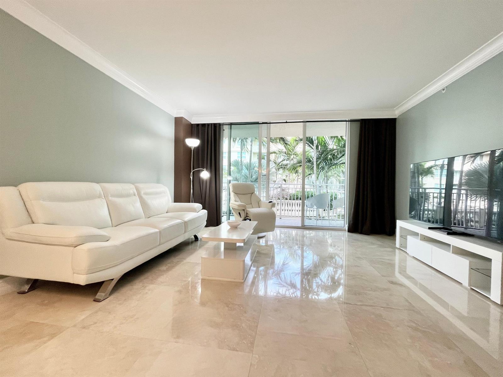 A living room features a white leather sofa, marble floors, and a sliding glass balcony door — 99 SE Mizner Boulevard # 736, Boca Raton FL 33432, BOCA RATON, FL