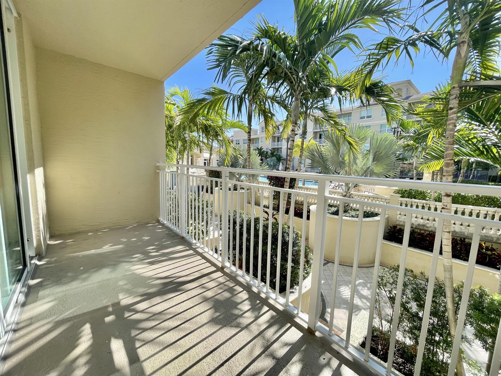 A covered balcony with a white metal railing overlooks a landscaped courtyard with palm trees — 99 SE Mizner Boulevard # 736, Boca Raton FL 33432, BOCA RATON, FL