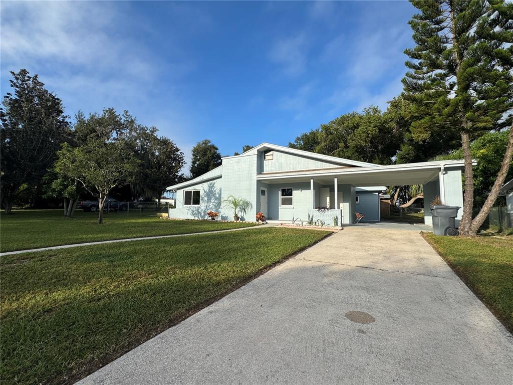 A light blue single-story house with a concrete driveway and attached carport under a blue sky — 2221 20TH STREET NW, WINTER HAVEN, FL