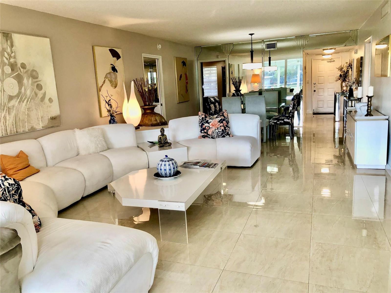 A bright living room features a white sectional sofa, glossy tile floors, and mirrored walls — 800 Cypress Grove Drive # 204, Pompano Beach FL 33069, POMPANO BEACH, FL