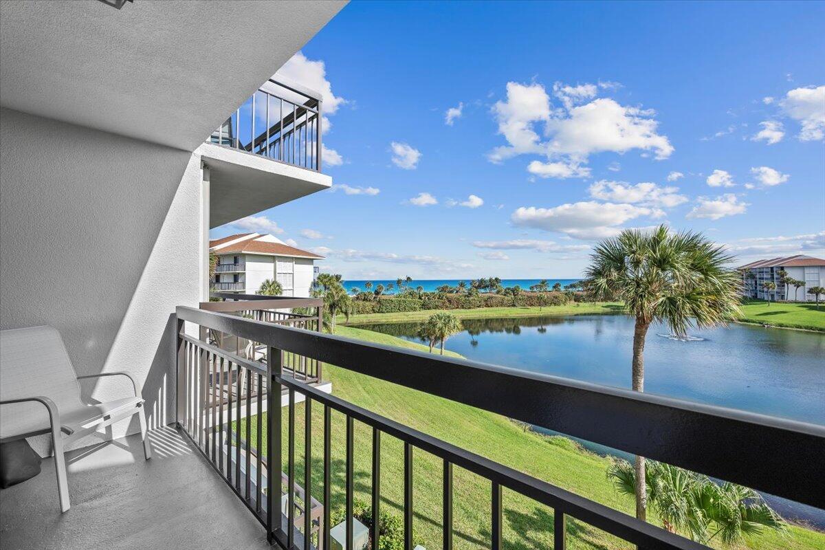 A balcony with a black railing overlooks a pond, green lawn, and the distant ocean — 201 S Seas Drive # 404, Jupiter FL 33477, JUPITER, FL