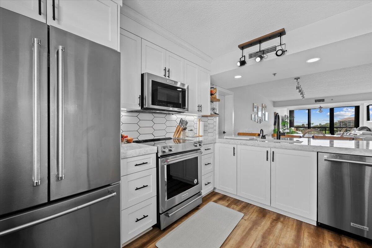 A modern kitchen features white cabinetry, stainless steel appliances, and a white tile backsplash — 201 S Seas Drive # 404, Jupiter FL 33477, JUPITER, FL