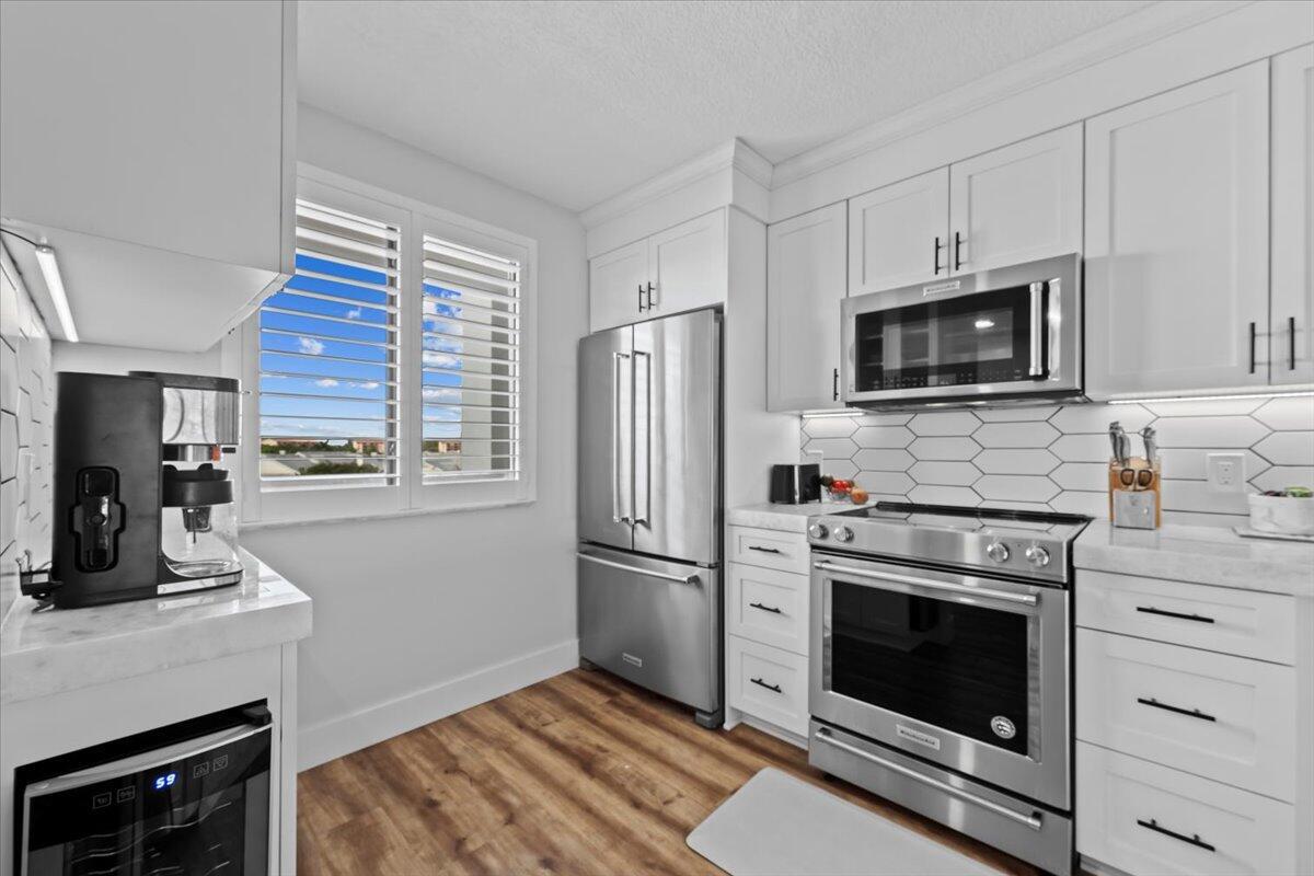 A modern kitchen features white cabinetry, stainless steel appliances, and a wood-look floor — 201 S Seas Drive # 404, Jupiter FL 33477, JUPITER, FL