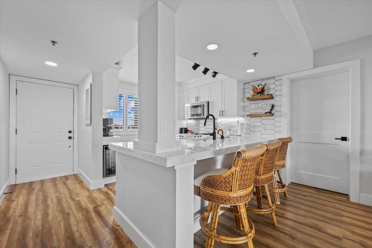 A kitchen features a white island with bar stools, light wood flooring, and white cabinetry — 201 S Seas Drive # 404, Jupiter FL 33477, JUPITER, FL