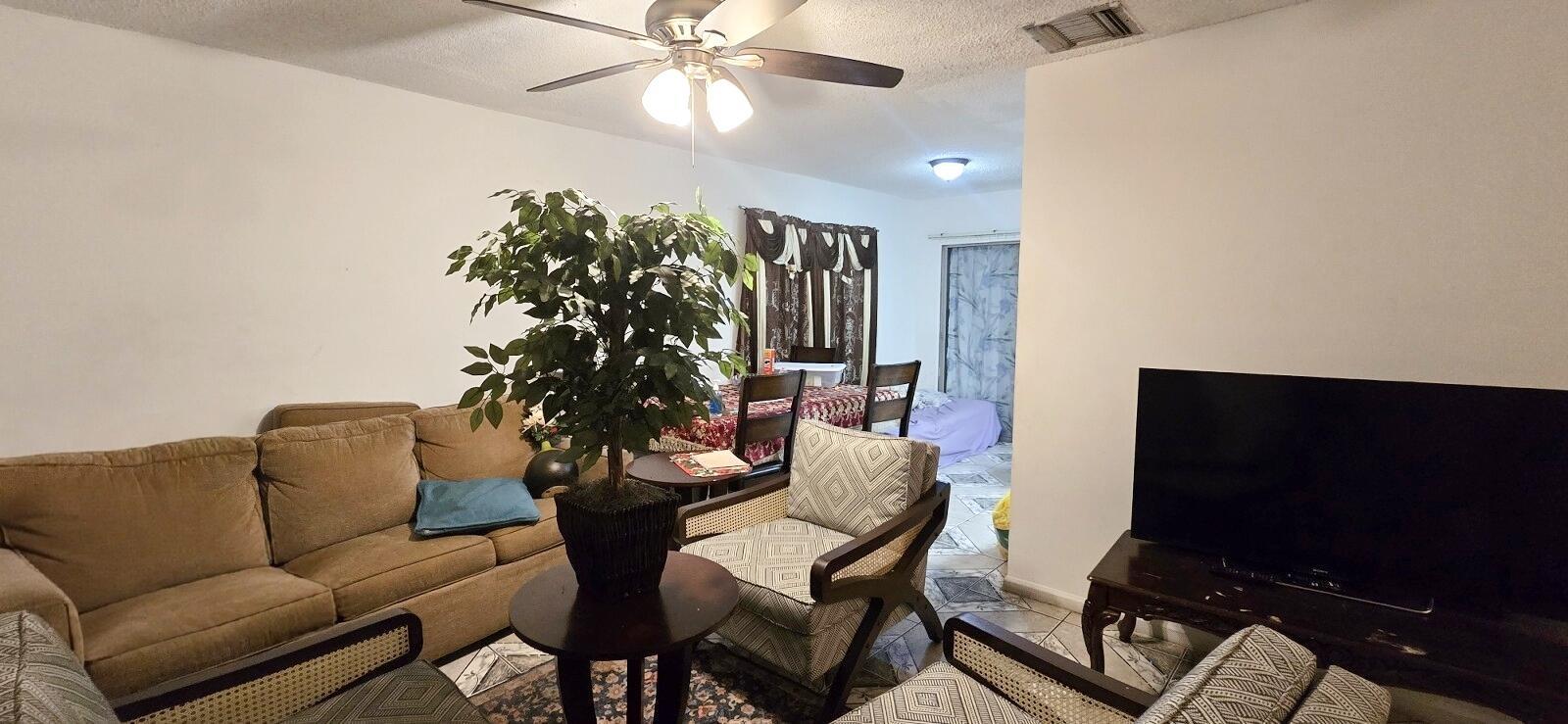 A living room with a brown sofa, patterned armchairs, a large plant, and a television — 233 SE 26th Avenue, Boynton Beach FL 33435, BOYNTON BEACH, FL