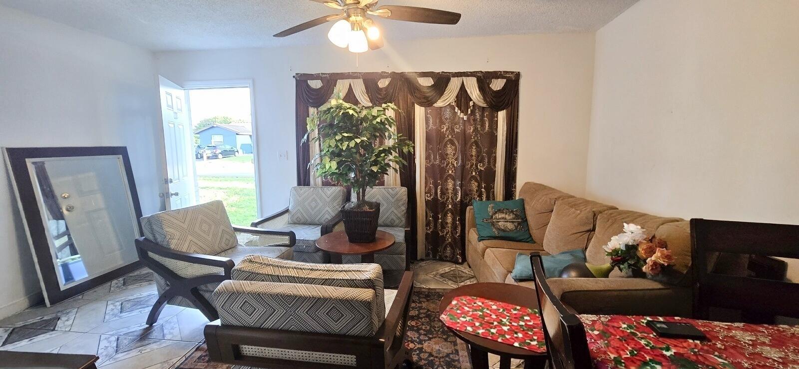 A living room features a tan sofa, patterned armchairs, a ceiling fan, and tile flooring — 233 SE 26th Avenue, Boynton Beach FL 33435, BOYNTON BEACH, FL