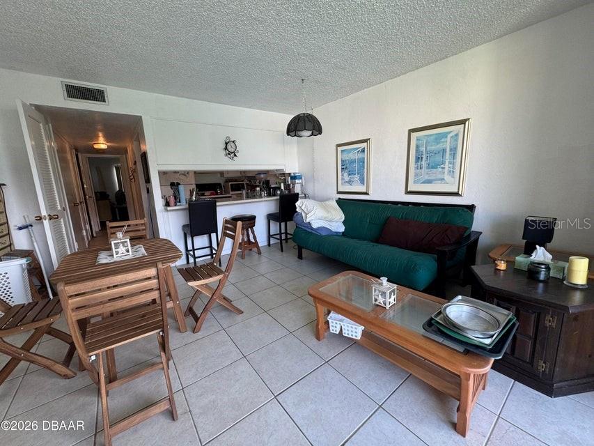 A living room and dining area feature tile flooring, a green futon, and a breakfast bar — 1441 N ATLANTIC AVENUE UNIT 216, DAYTONA BEACH, FL