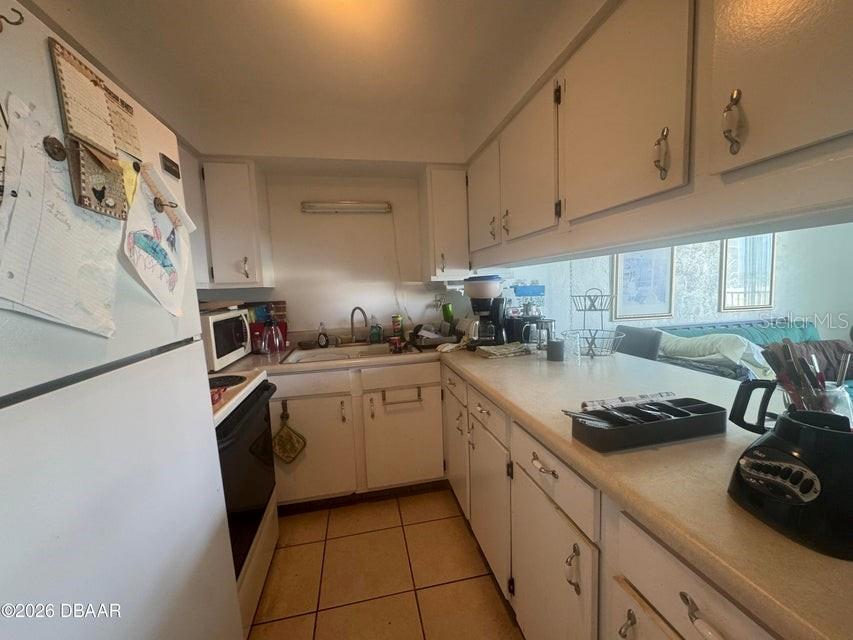A kitchen features white cabinets, light countertops, a tiled floor, and a pass-through window — 1441 N ATLANTIC AVENUE UNIT 216, DAYTONA BEACH, FL