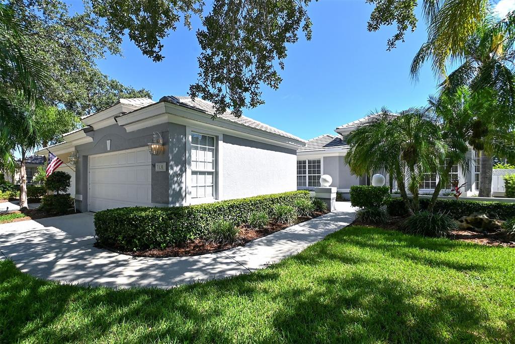 A single-story gray house with a white garage door, manicured hedges, and palm trees — 7131 KENSINGTON COURT, UNIVERSITY PARK, FL