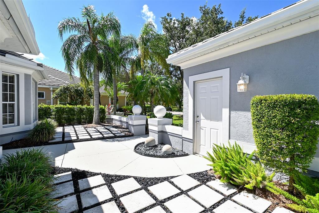 A paved courtyard with square stepping stones, palm trees, and a white exterior door — 7131 KENSINGTON COURT, UNIVERSITY PARK, FL