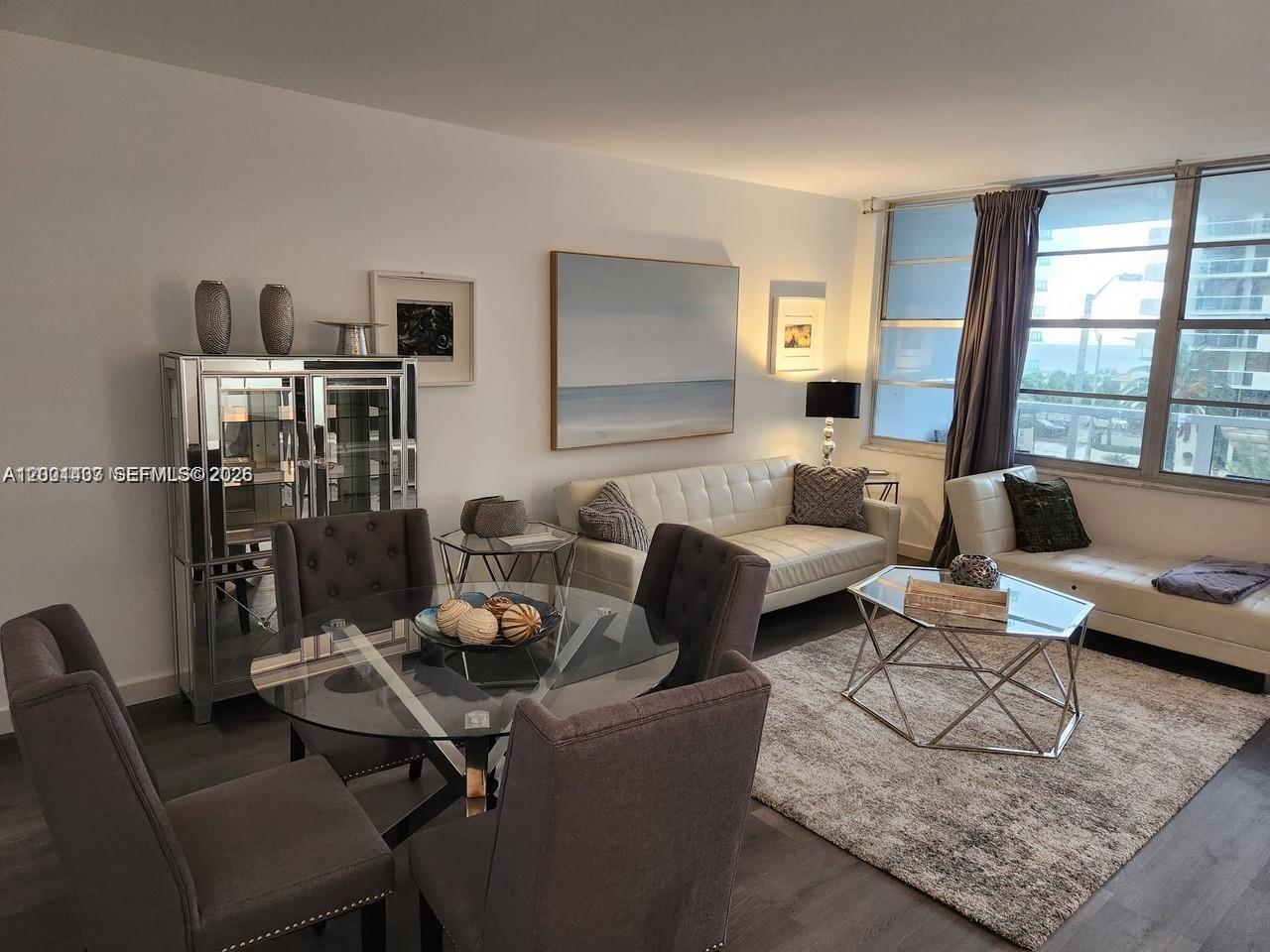 A living and dining area features a glass table, grey chairs, and white sofas — 5700 Collins Ave # 4N, Miami Beach FL 33140, MIAMI BEACH, FL