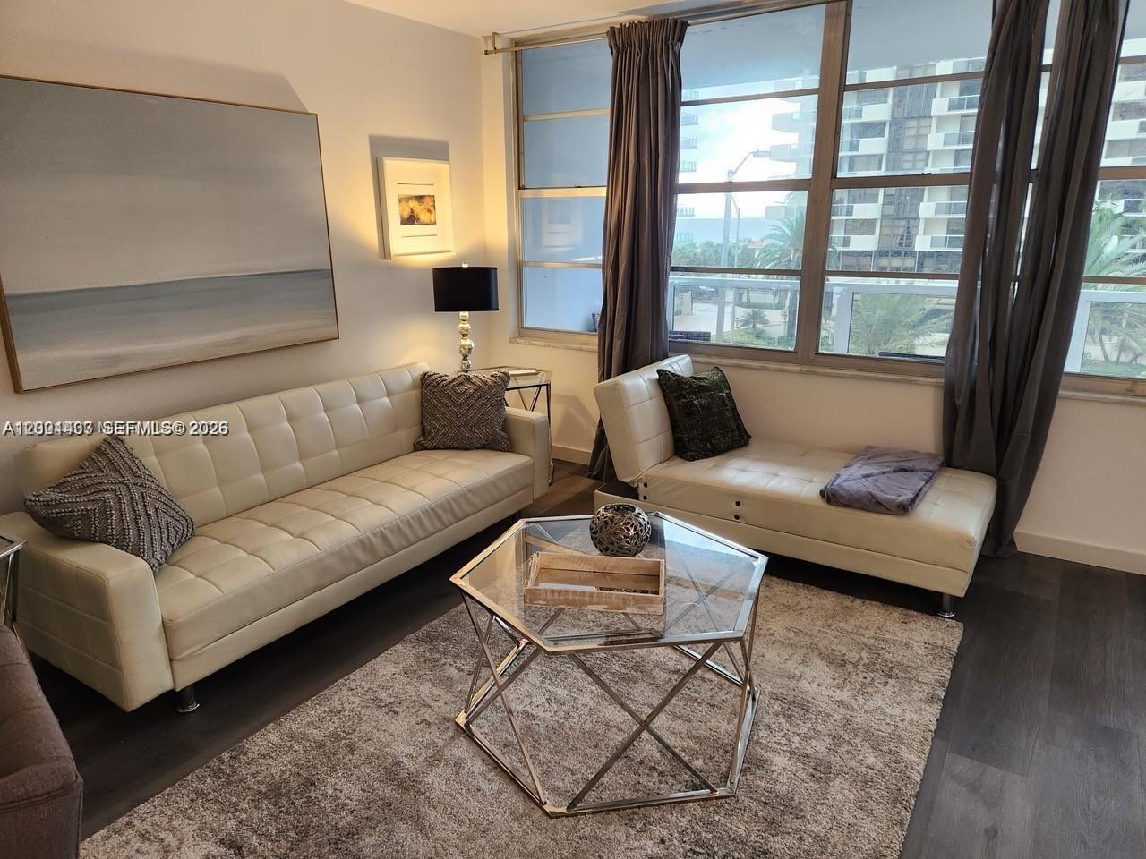 A living room features a white tufted sofa, a chaise lounge, and a glass coffee table — 5700 Collins Ave # 4N, Miami Beach FL 33140, MIAMI BEACH, FL