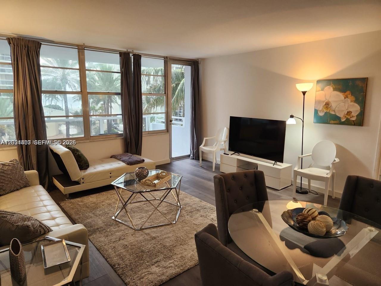 A living room features a glass coffee table, white sofa, television, and large windows — 5700 Collins Ave # 4N, Miami Beach FL 33140, MIAMI BEACH, FL
