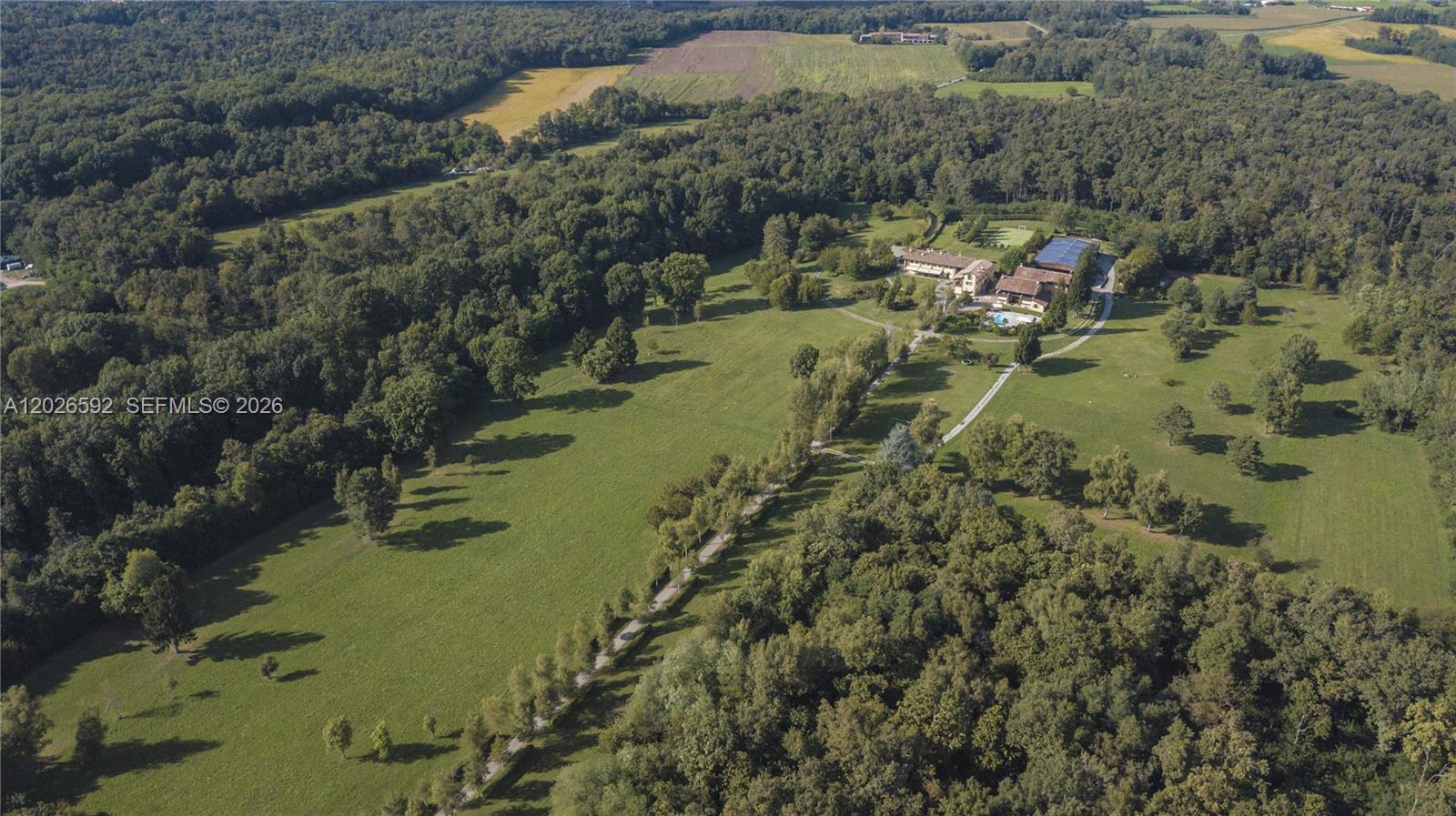 An aerial view shows a large estate with a house, pool, and driveway amidst fields — Lombardia Venegono Superiore, VA 20100, VA