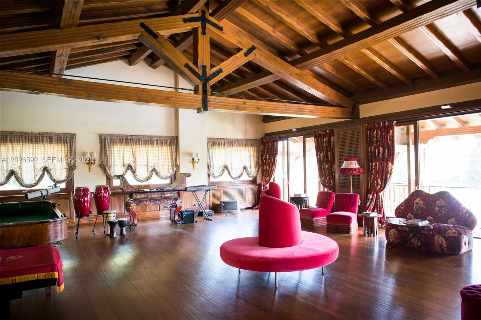 A spacious room features exposed wooden ceiling beams, hardwood floors, and eclectic red furniture — Lombardia Venegono Superiore, VA 20100, VA