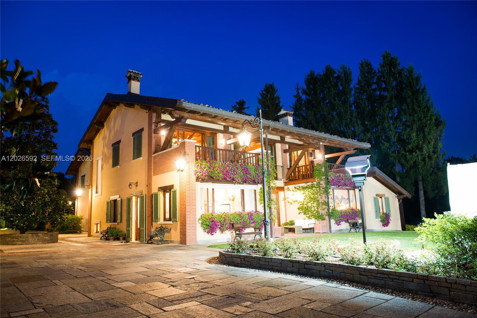 A two-story house with a stone patio, brick accents, and flower-covered balconies at night — Lombardia Venegono Superiore, VA 20100, VA