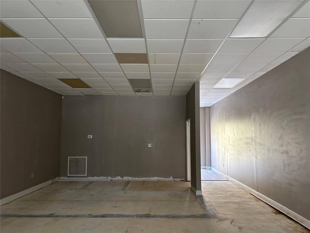 An empty commercial space features gray walls, a drop ceiling, and unfinished concrete flooring — 5132 LAND O LAKES BOULEVARD UNIT 105, LAND O LAKES, FL