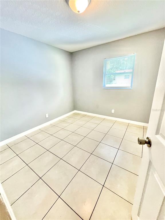 A small, empty room features light gray walls, white trim, and beige tiled flooring — 403 TERRY STREET, WILDWOOD, FL