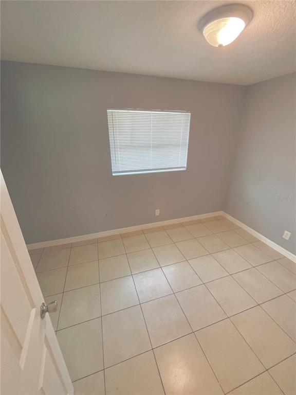 An empty bedroom with light gray walls, beige tile flooring, and a single window — 403 TERRY STREET, WILDWOOD, FL
