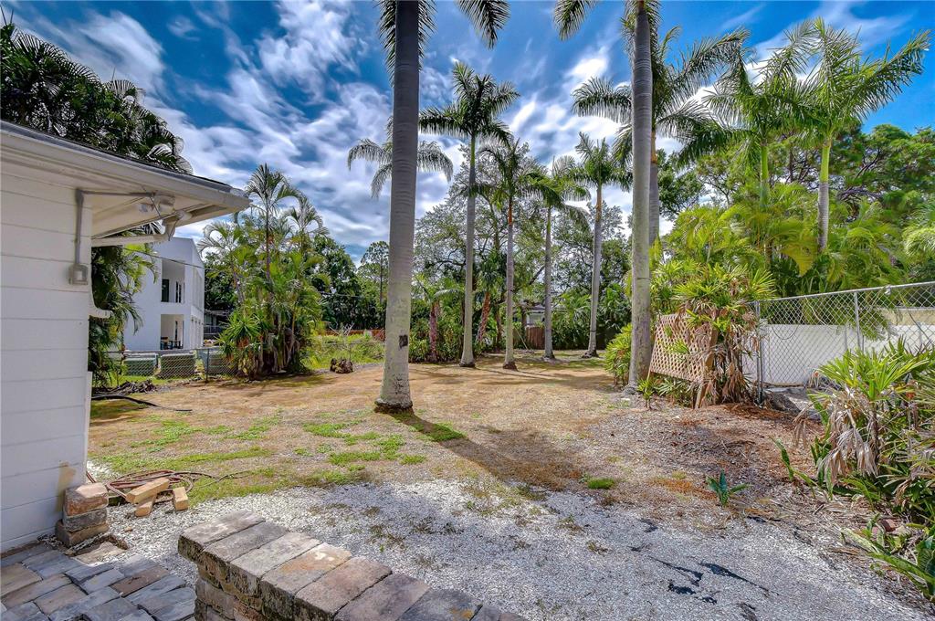 A backyard with a gravel patio, a brick wall, and several tall palm trees — 5006 W DICKENS AVENUE, TAMPA, FL