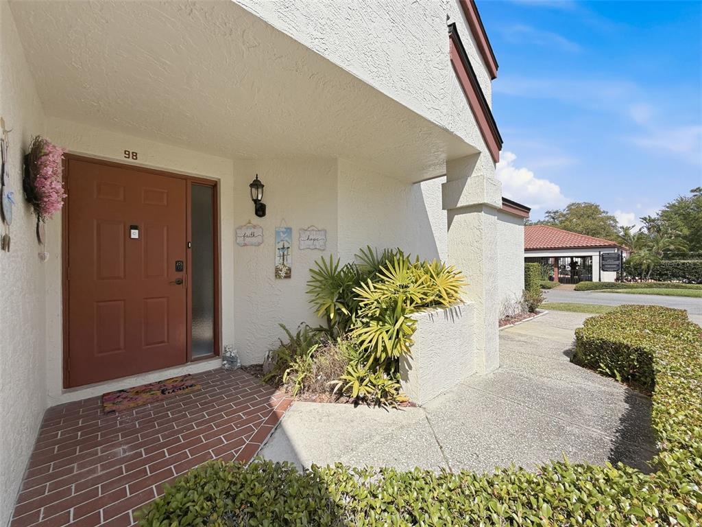 The exterior entrance features a red door, brick flooring, and a small garden bed — 3455 COUNTRYSIDE BOULEVARD UNIT 98, CLEARWATER, FL