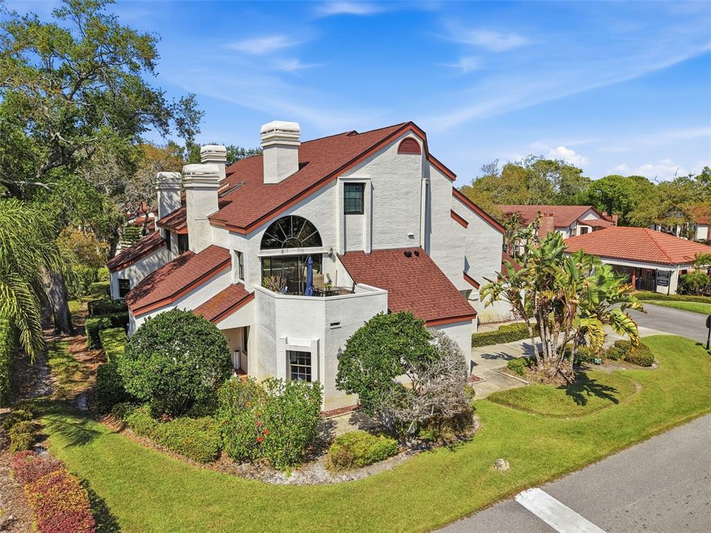 An exterior view of a multi-story white stucco townhouse with a red shingled roof — 3455 COUNTRYSIDE BOULEVARD UNIT 98, CLEARWATER, FL