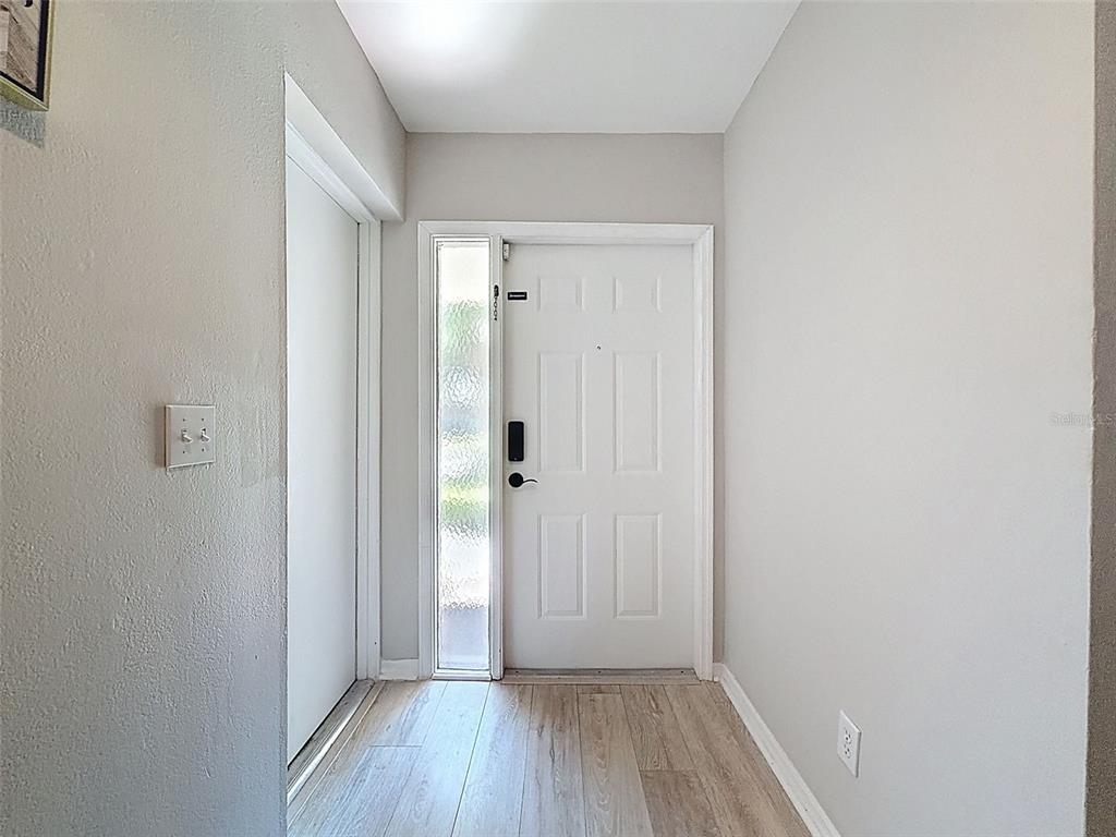 A white front door with a side window and light wood-look flooring in an entryway — 3455 COUNTRYSIDE BOULEVARD UNIT 98, CLEARWATER, FL