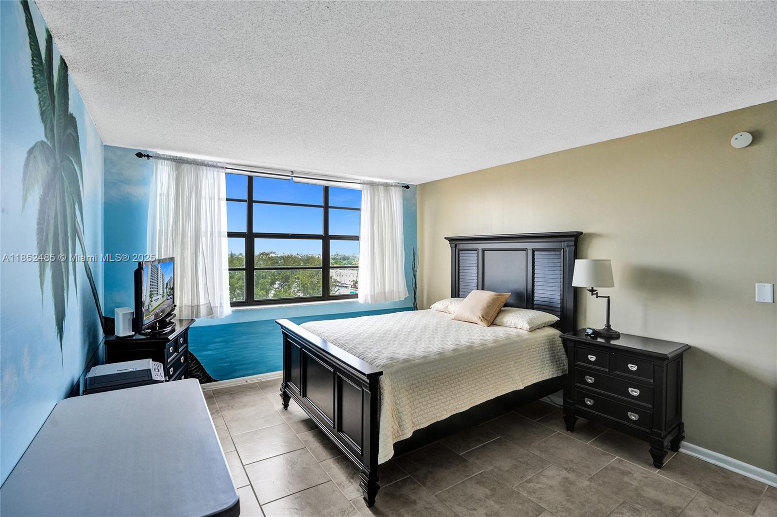 A bedroom features a dark wood bed frame, tile flooring, and a wall mural — 1401 N Riverside Dr # 1005, Pompano Beach FL 33062, POMPANO BEACH, FL
