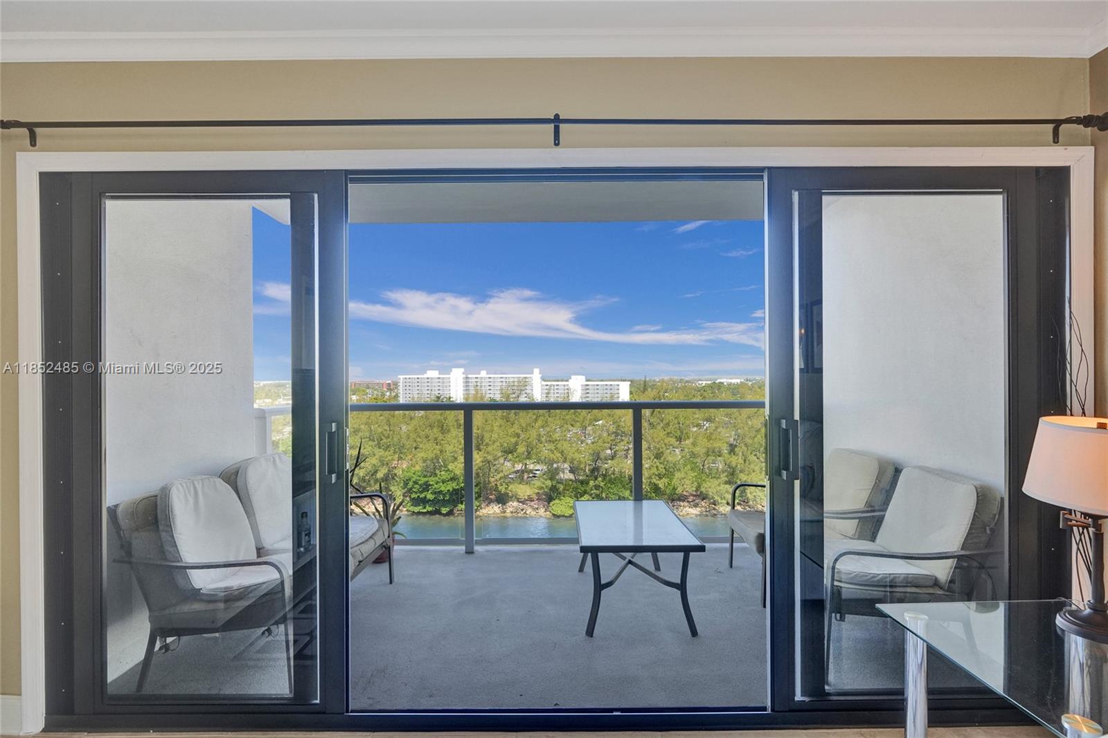 A balcony with patio furniture overlooks a river and distant buildings through sliding glass doors — 1401 N Riverside Dr # 1005, Pompano Beach FL 33062, POMPANO BEACH, FL
