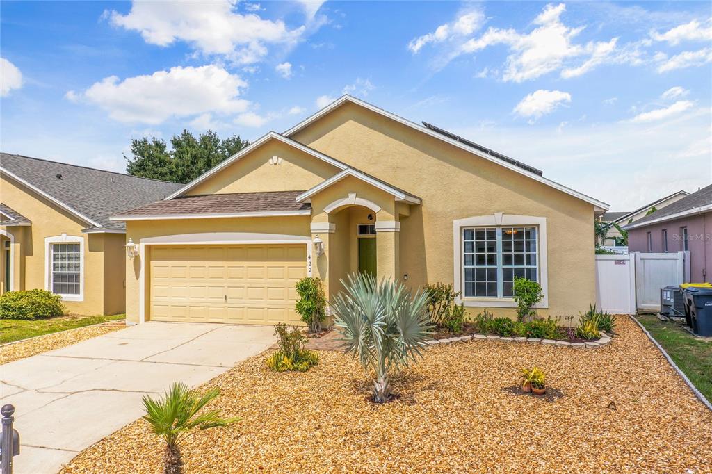 A single-story house with a tan stucco exterior, a two-car garage, and a gravel front yard — 422 GRAYSTONE BOULEVARD, DAVENPORT, FL