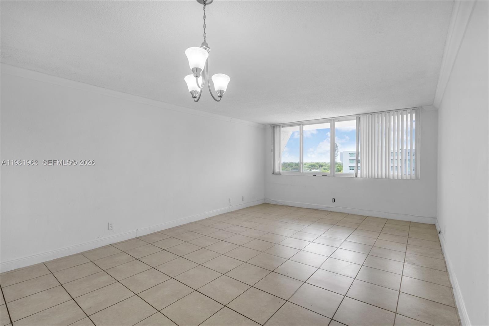 An empty room features white walls, a tiled floor, and a three-light chandelier — 9143 SW 77th Ave # B710, Miami FL 33156, MIAMI, FL