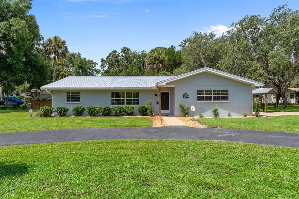 A single-story house with a light gray exterior, metal roof, and a curved asphalt driveway — 914 N MCGOWAN AVENUE, CRYSTAL RIVER, FL