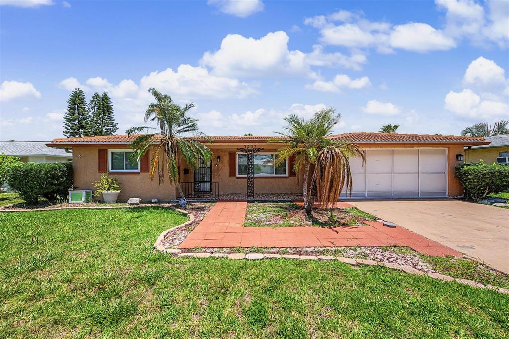 A single-story house with a tan stucco exterior, a tile roof, and a palm-lined front yard — 3837 TOPSAIL TRAIL, NEW PORT RICHEY, FL