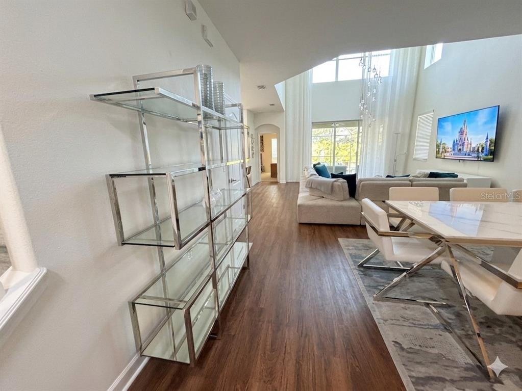 A modern living and dining area features a glass shelving unit, wood floors, and high ceilings — 2997 BUCCANEER PALM ROAD, KISSIMMEE, FL