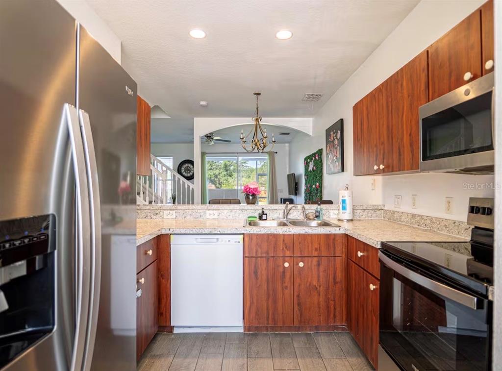 A kitchen with wood cabinets, stainless steel appliances, and a view into the living area — 1160 S BEACH CIRCLE, KISSIMMEE, FL