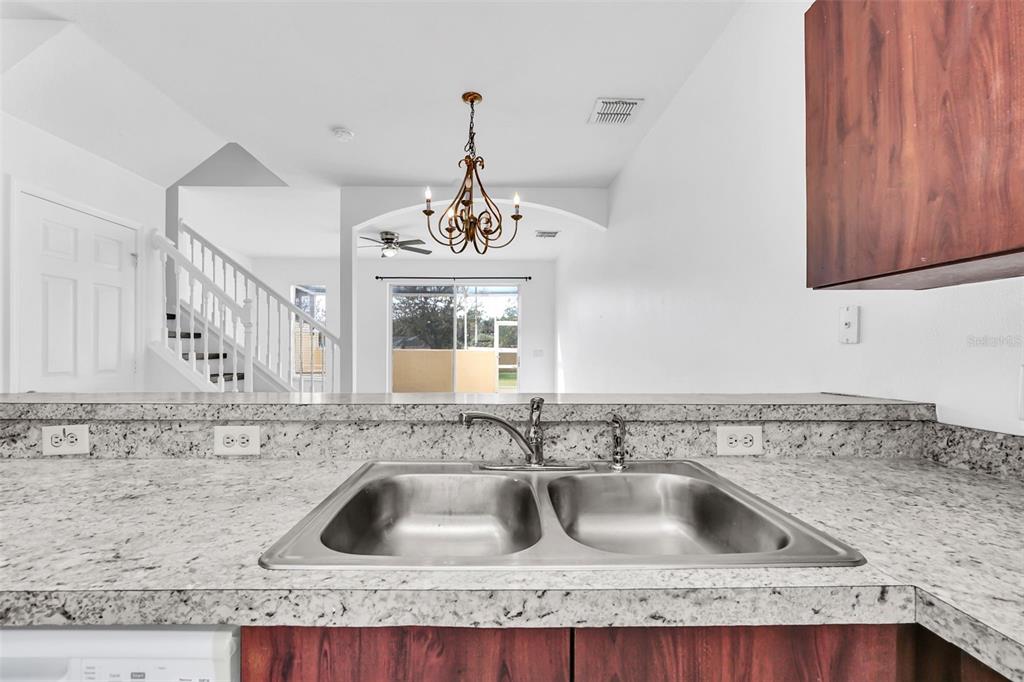 A kitchen sink with granite countertops overlooks a living area with a staircase and chandelier — 1160 S BEACH CIRCLE, KISSIMMEE, FL