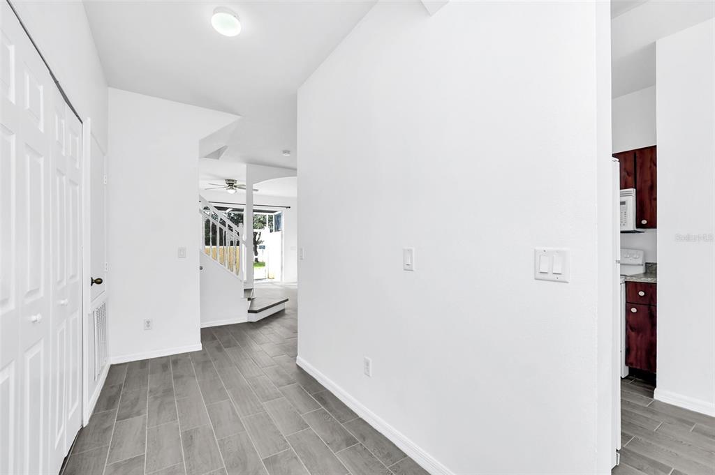 A hallway with gray tile flooring leads toward a staircase and a kitchen area — 1160 S BEACH CIRCLE, KISSIMMEE, FL