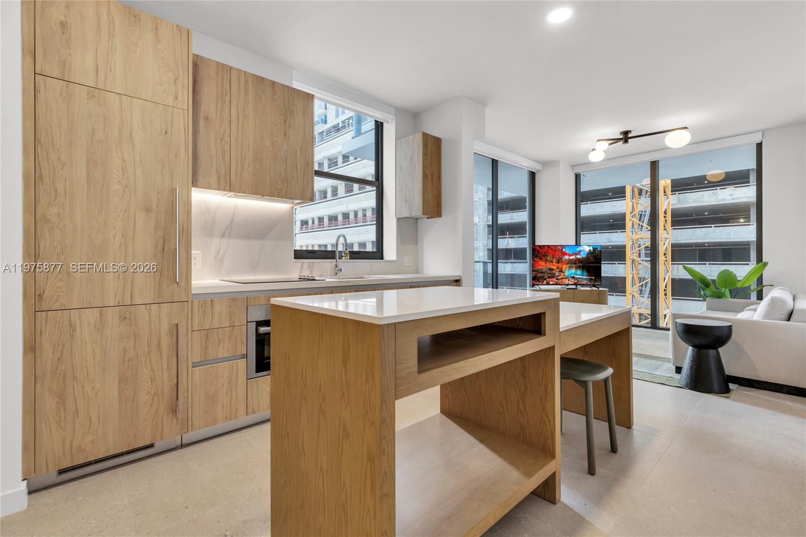 A modern kitchen features light wood cabinetry, a central island, and floor-to-ceiling windows — 11 NE 6th St # 407, Miami FL 33132, MIAMI, FL