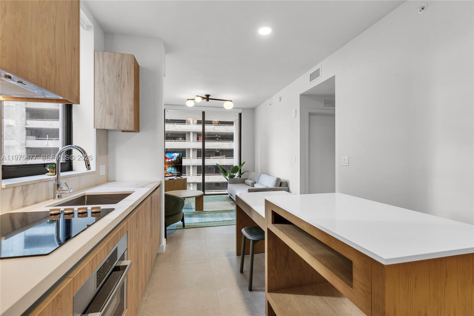 A modern kitchen with wood cabinetry and white countertops opens into a living area — 11 NE 6th St # 407, Miami FL 33132, MIAMI, FL