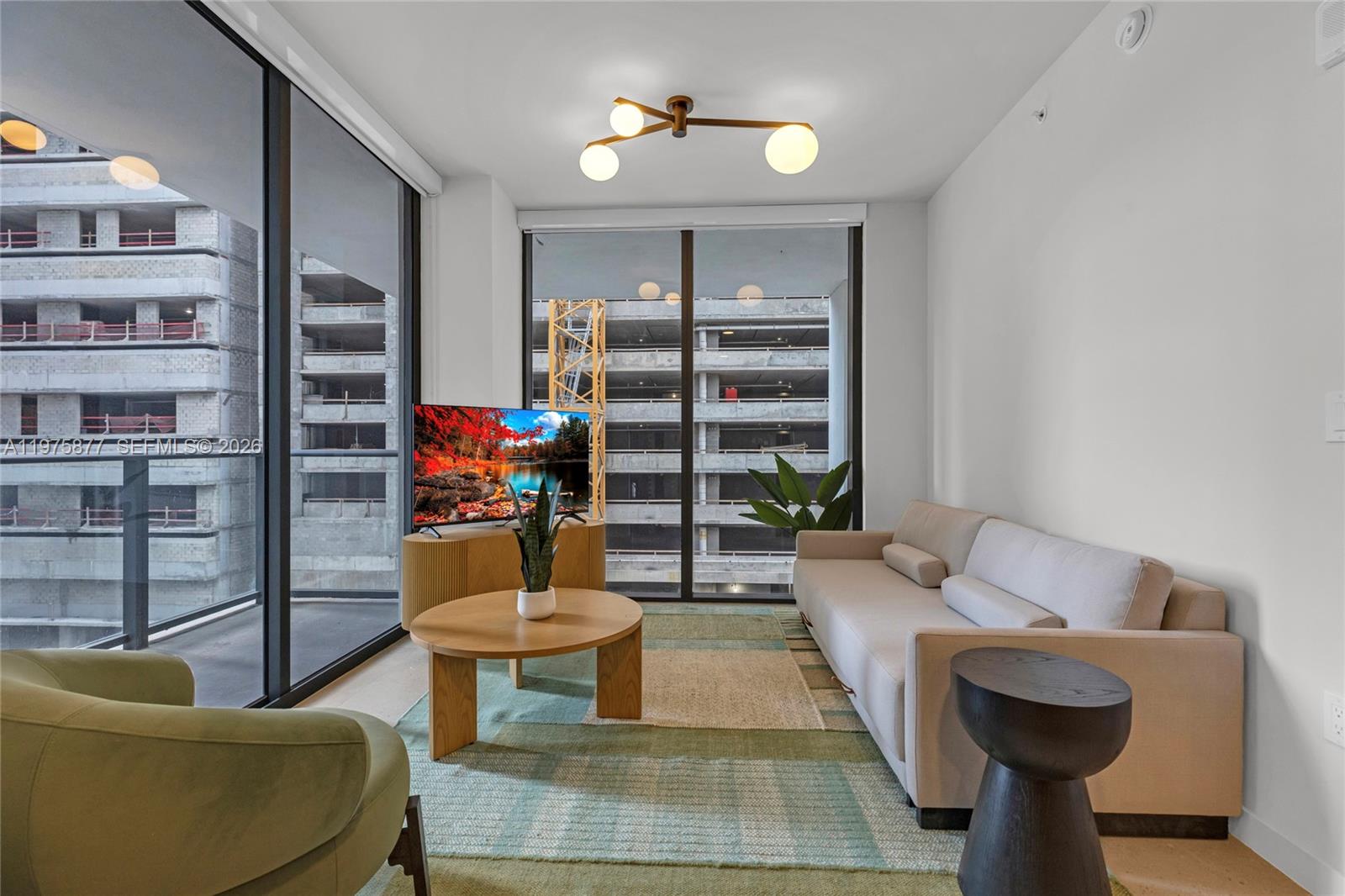A living room features a beige sofa, round coffee table, and floor-to-ceiling windows overlooking construction — 11 NE 6th St # 407, Miami FL 33132, MIAMI, FL
